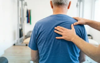 Posture treatment specialist in Los Angeles assessing an older man's upper back and shoulder alignment to help improve comfort and movement.